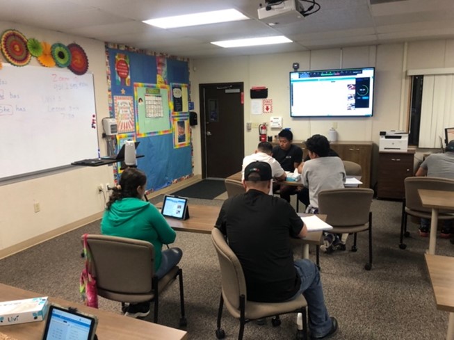 Classroom setting, students sitting behind a desk involved in a discussion