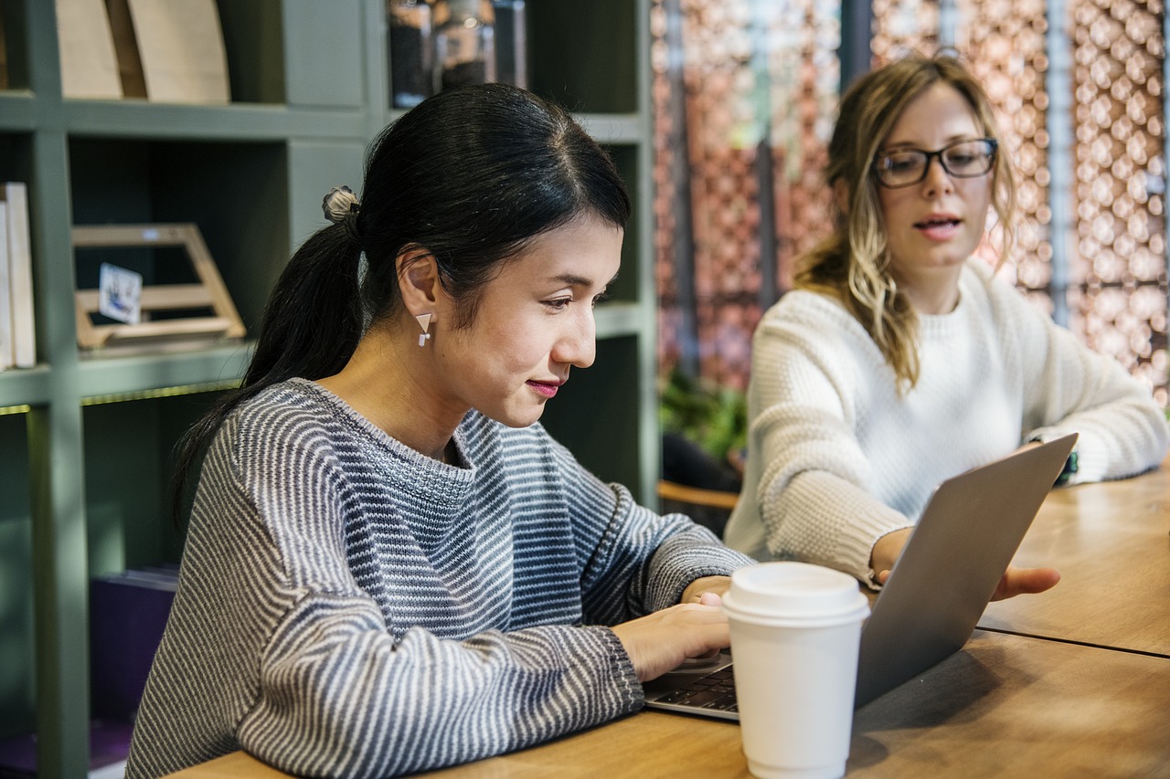 Two women sitting at desk with laptop open.