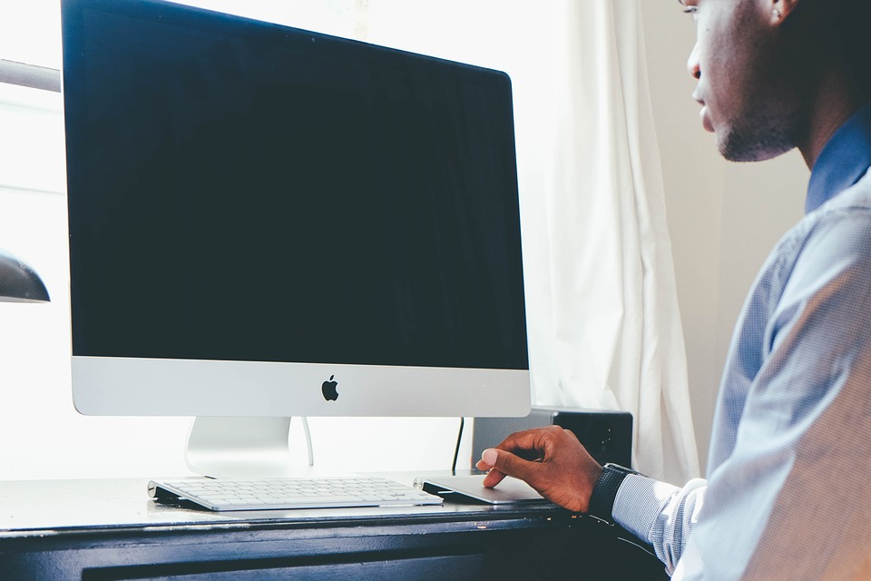 Man sitting in front of a large computer screen with finger on track pad